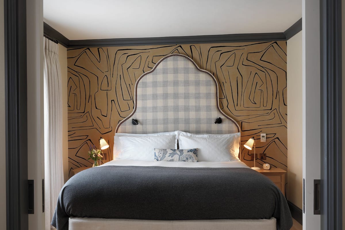 A modern bedroom with a large bed, a headboard with a geometric pattern, bedside lamps, and a nightstand with a clock.