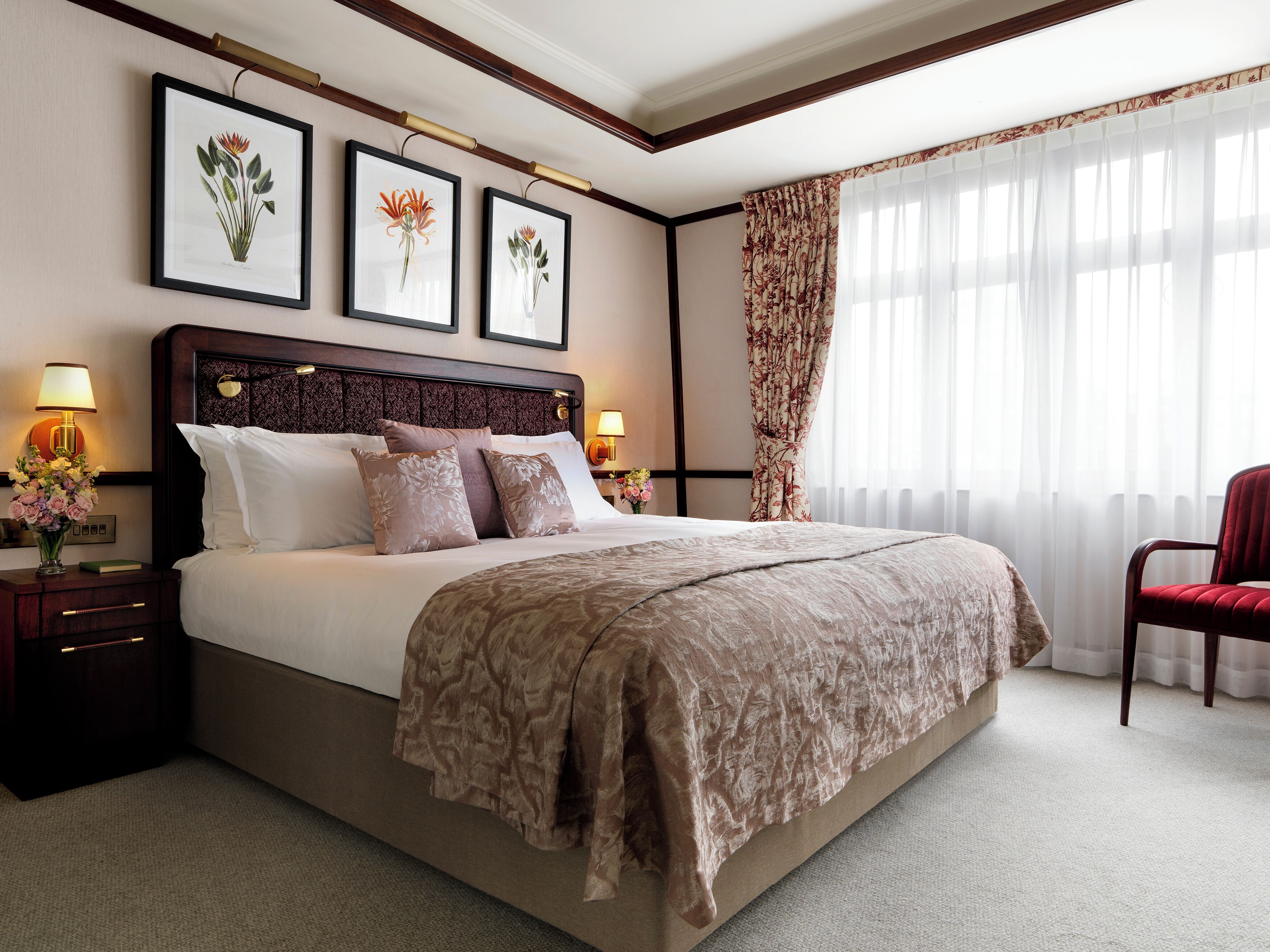 Ein Hotelzimmer mit einem großen Bett, einem Nachttisch mit Lampe, einem Sessel und gerahmten Pflanzenbildern an der Wand.