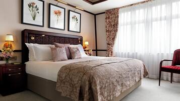 Ein Hotelzimmer mit einem großen Bett, einem Nachttisch mit Lampe, einem Sessel und gerahmten Pflanzenbildern an der Wand.