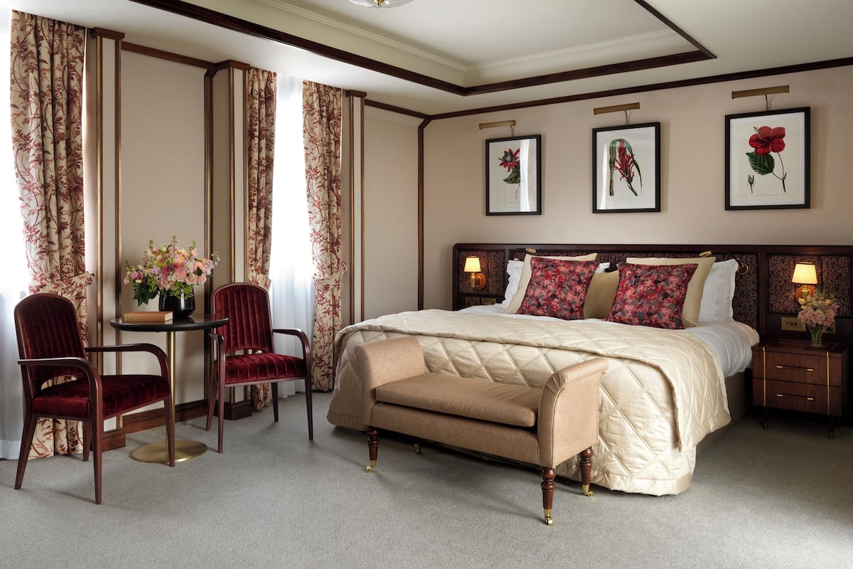 A spacious bedroom with a large bed, a sitting area with a chair and table, and floral curtains.
