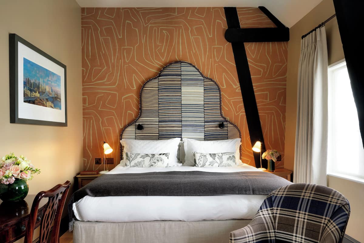 A neatly made bed with a striped headboard, a plaid armchair, and a framed picture on the wall.