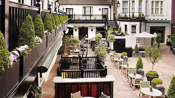 Un patio con mobiliario exterior, una escalera y edificios con balcones.