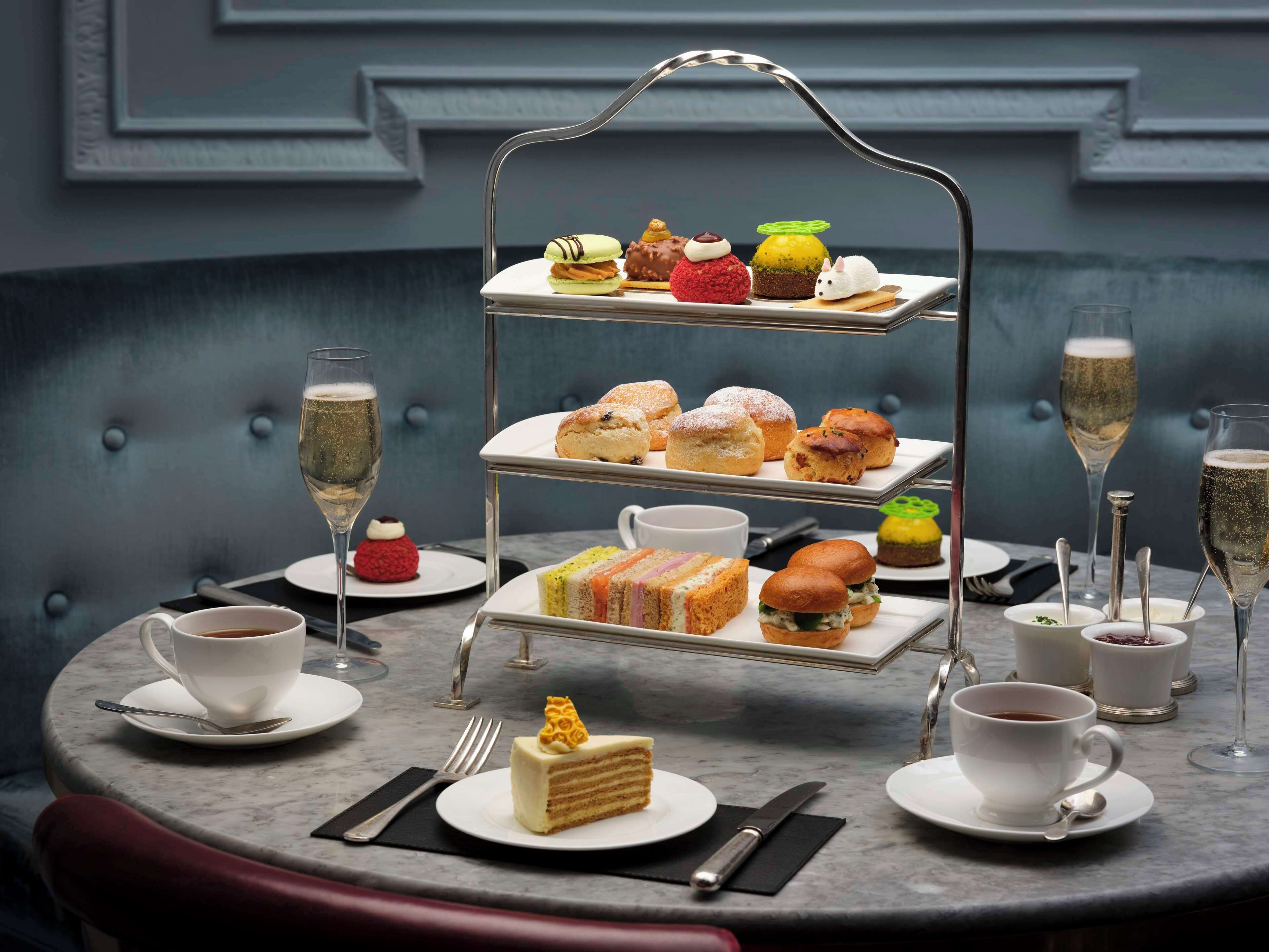 A three-tiered dessert display with various pastries and a cake, accompanied by cups of coffee and glasses of champagne on a marble table.