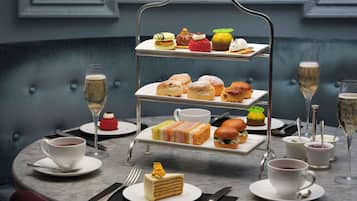 A three-tiered dessert display with various pastries and a cake, accompanied by cups of coffee and glasses of champagne on a marble table.