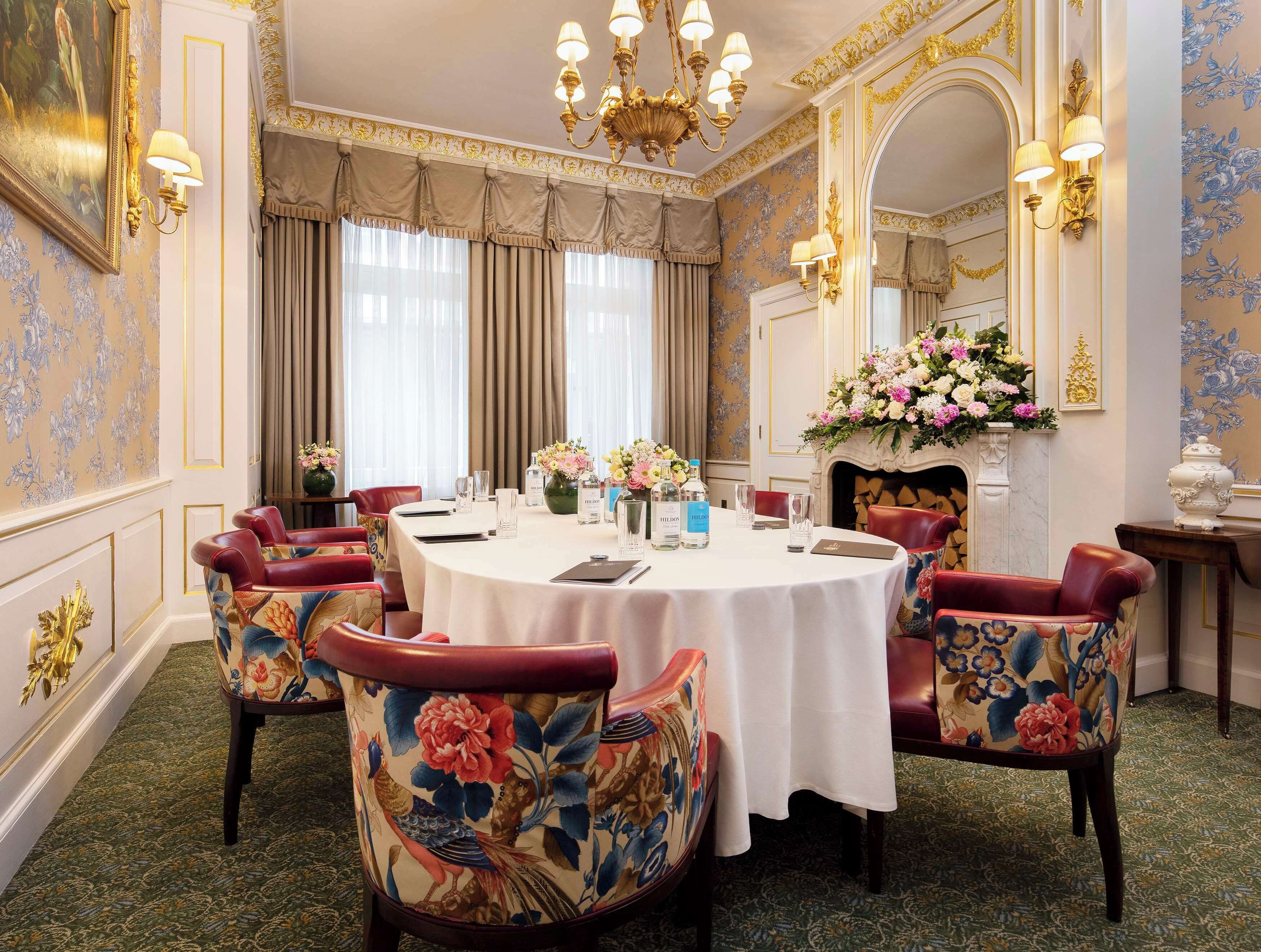 A formal dining room with a round table, floral chairs, and a chandelier.