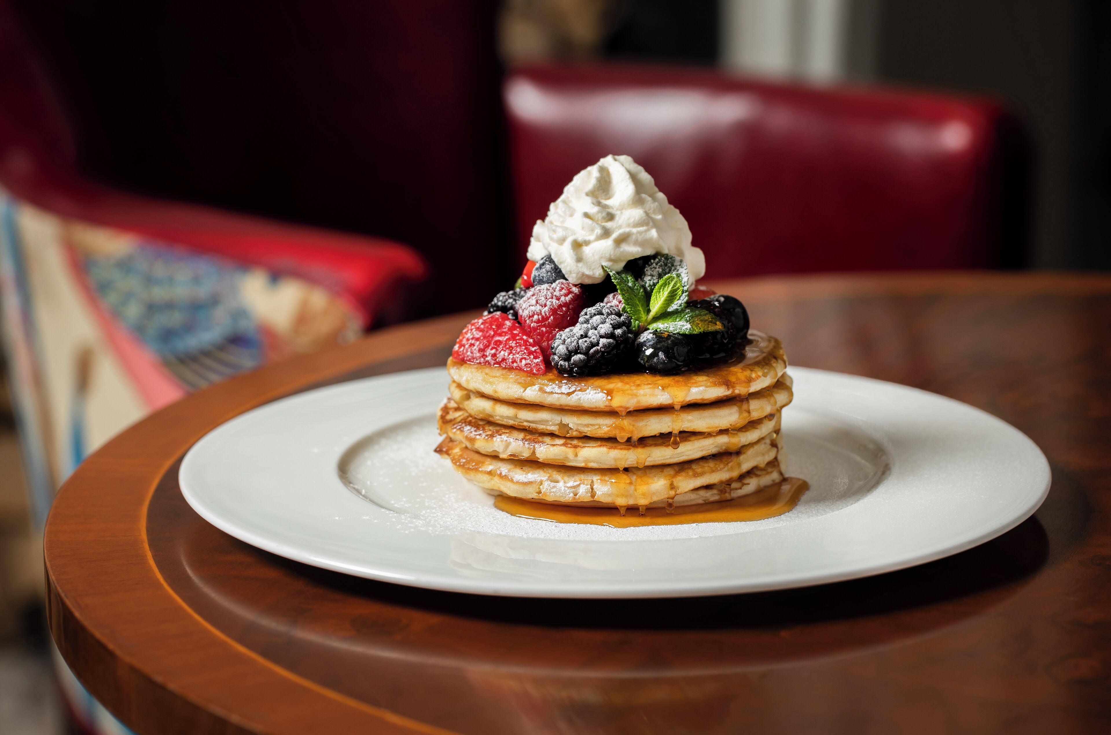 Una pila de panqueques con fruta y crema batida sobre un plato blanco.