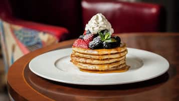 Una pila de panqueques con fruta y crema batida sobre un plato blanco.
