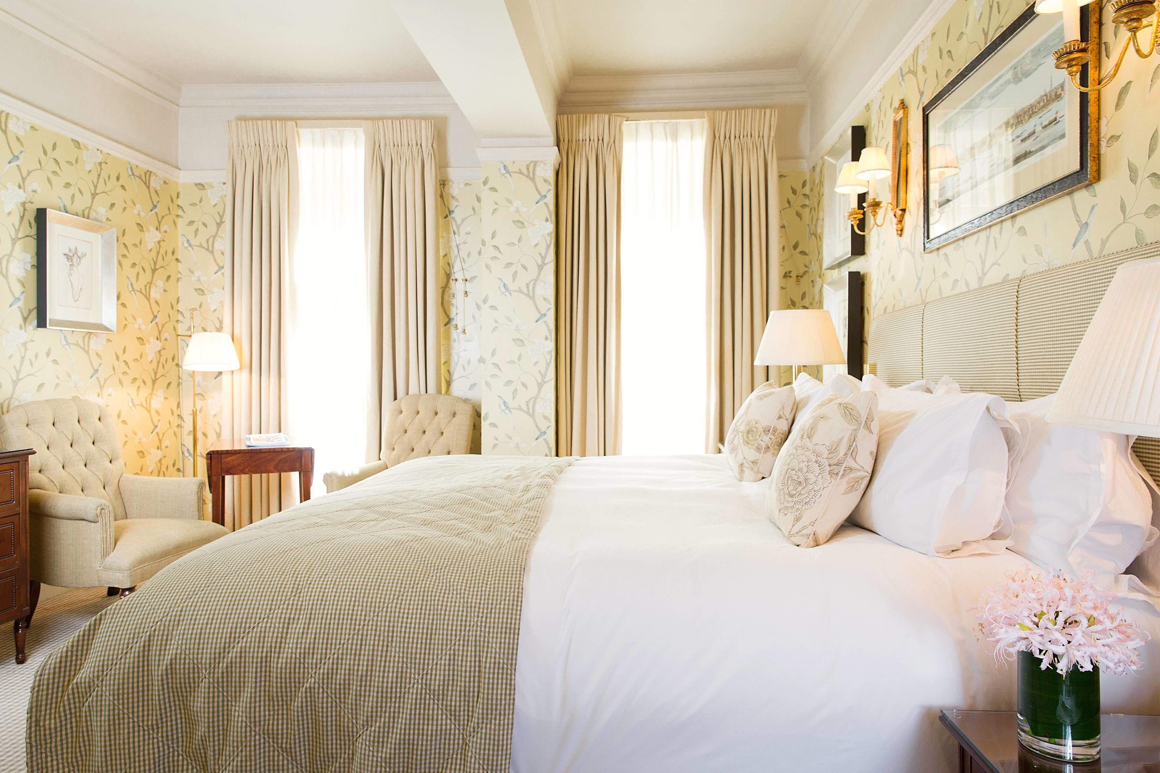 A hotel room with a large bed, a sitting area with a chair and a table, and a vase of flowers on a nightstand.