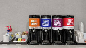 Cuatro dispensadores de café etiquetados como 'Light Roast', 'Dark Roast', 'Decaf Roast' y 'Agua Caliente', con varios pods de café y una botella de agua sobre una bandeja.