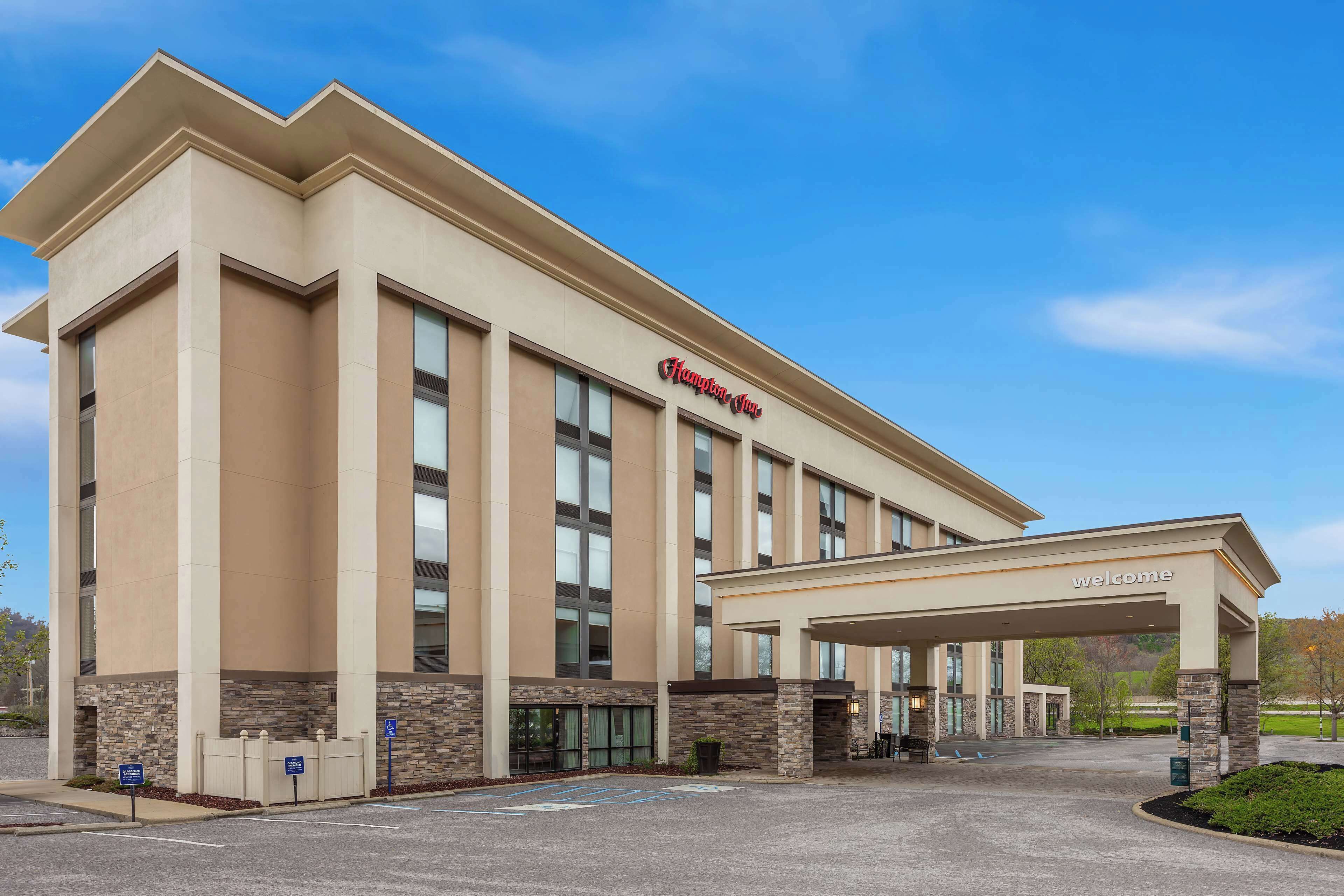 Un hotel moderno con un llamativo letrero de 'Hampton Inn', una entrada cubierta y un estacionamiento.