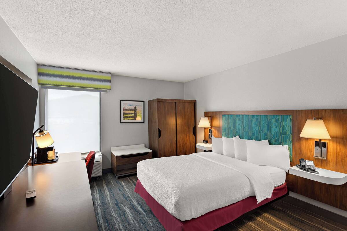 A hotel room with a bed, bedside tables, a desk, a chair, a wardrobe, and a window.
