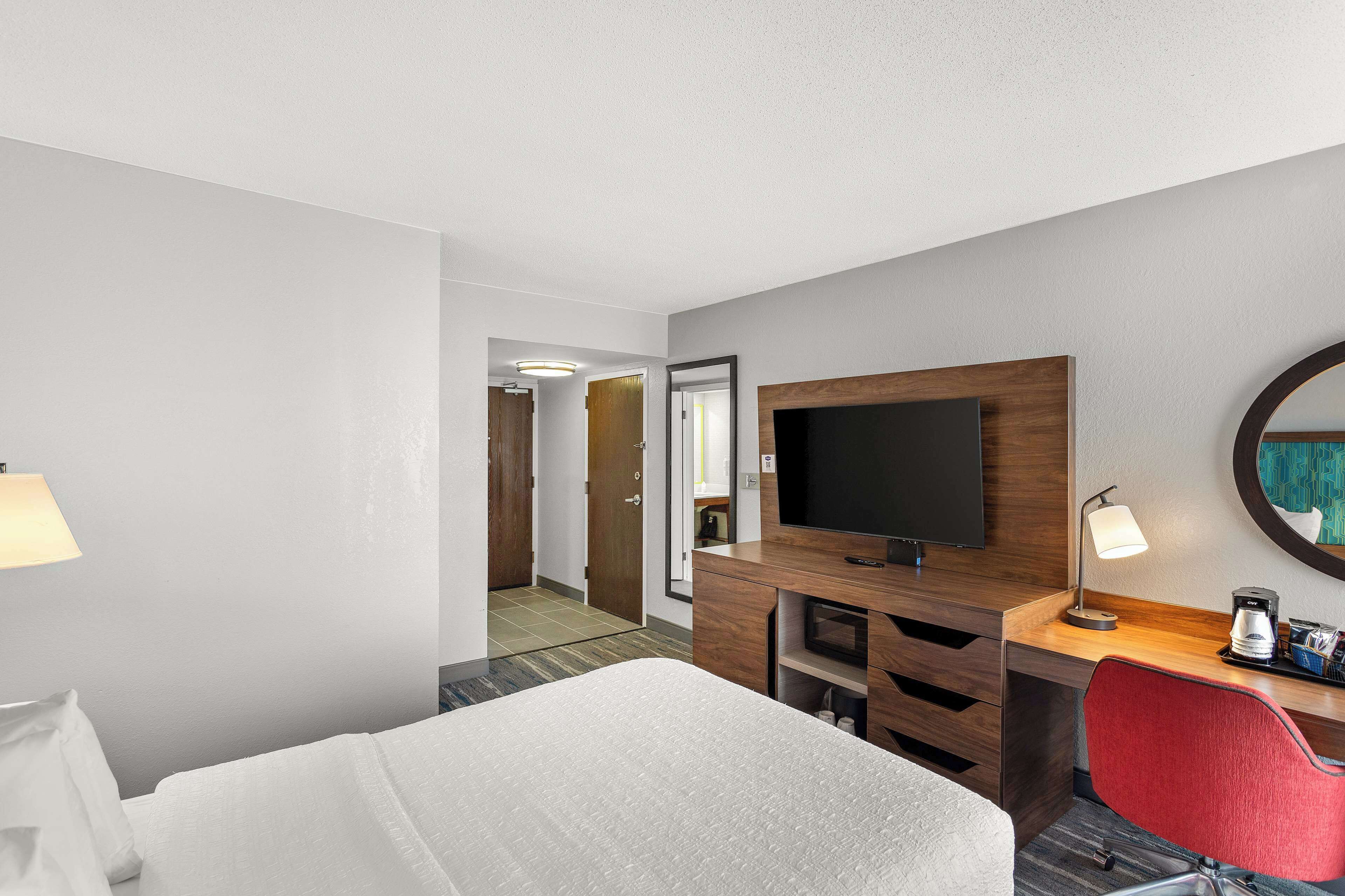 Una habitación de hotel con una cama, un escritorio con televisor, una silla y una lámpara.