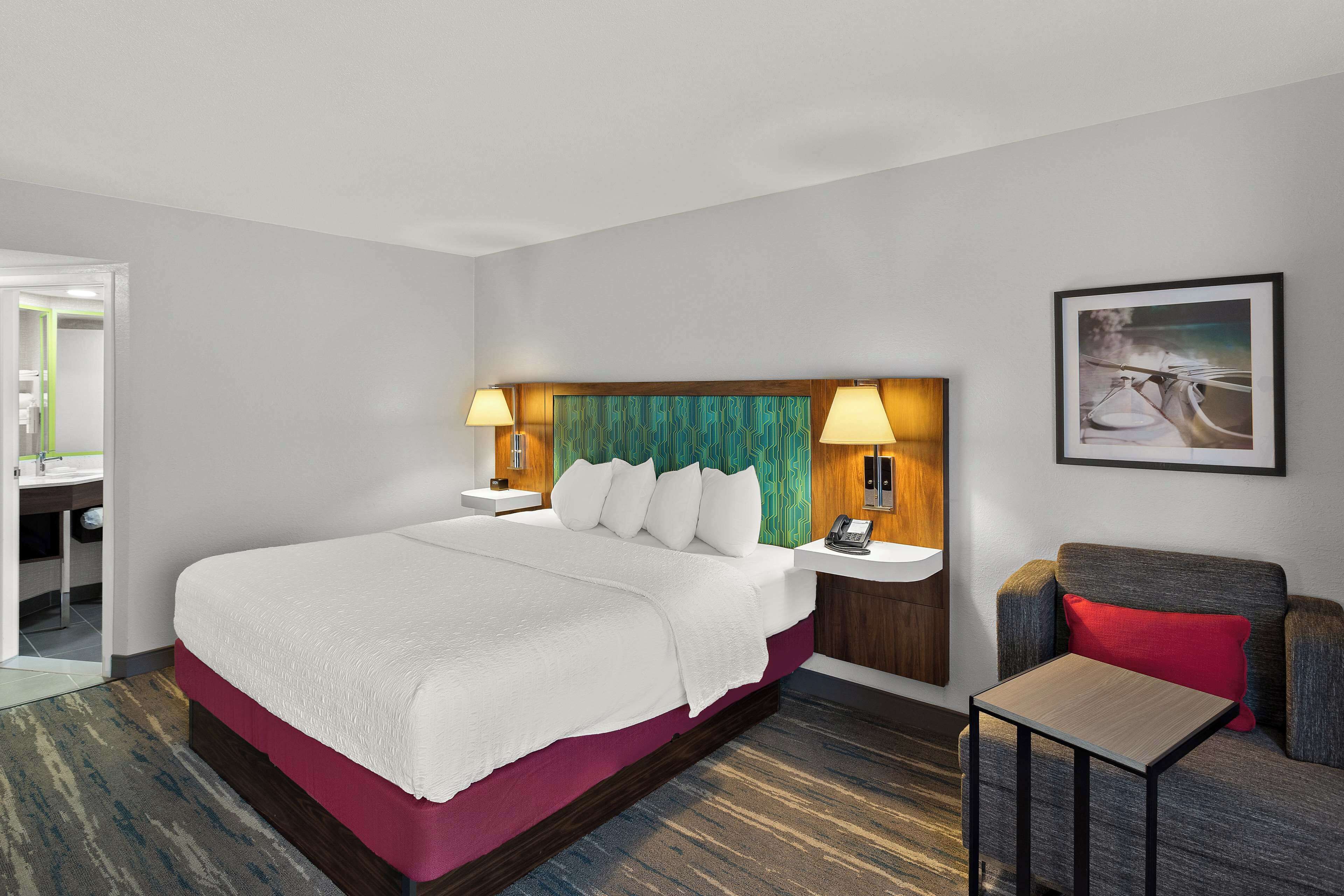 A hotel room with a large bed, bedside lamps, a small table, a sofa, and a painting on the wall.