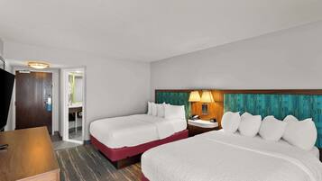 A hotel room with two beds, a desk, a nightstand, and a bathroom visible through an open door.