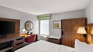Une chambre d’hôtel avec un lit, un bureau avec une télévision, une chaise rouge, une armoire en bois et une fenêtre donnant sur un paysage agréable.