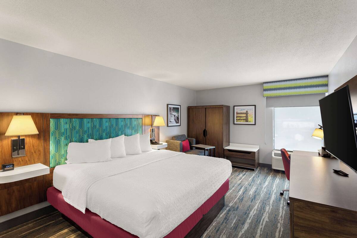 A hotel room with a large bed, a desk, a chair, a TV, and a window.