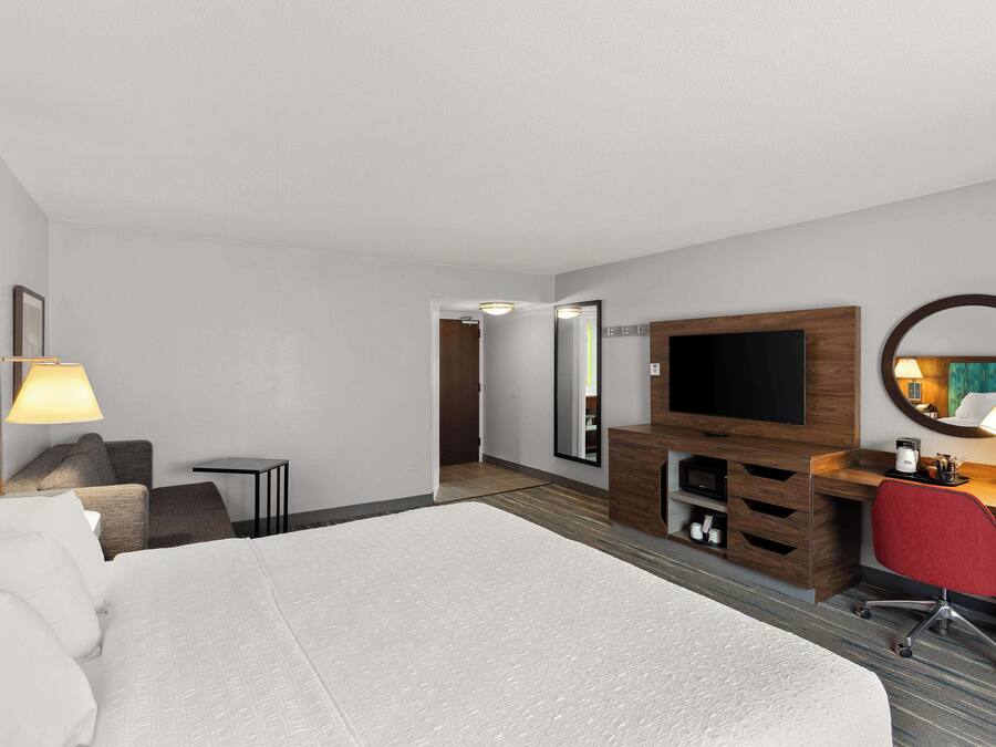 Camera d'albergo con un letto grande, una scrivania con una sedia, una TV, uno specchio e un tavolino con una lampada.