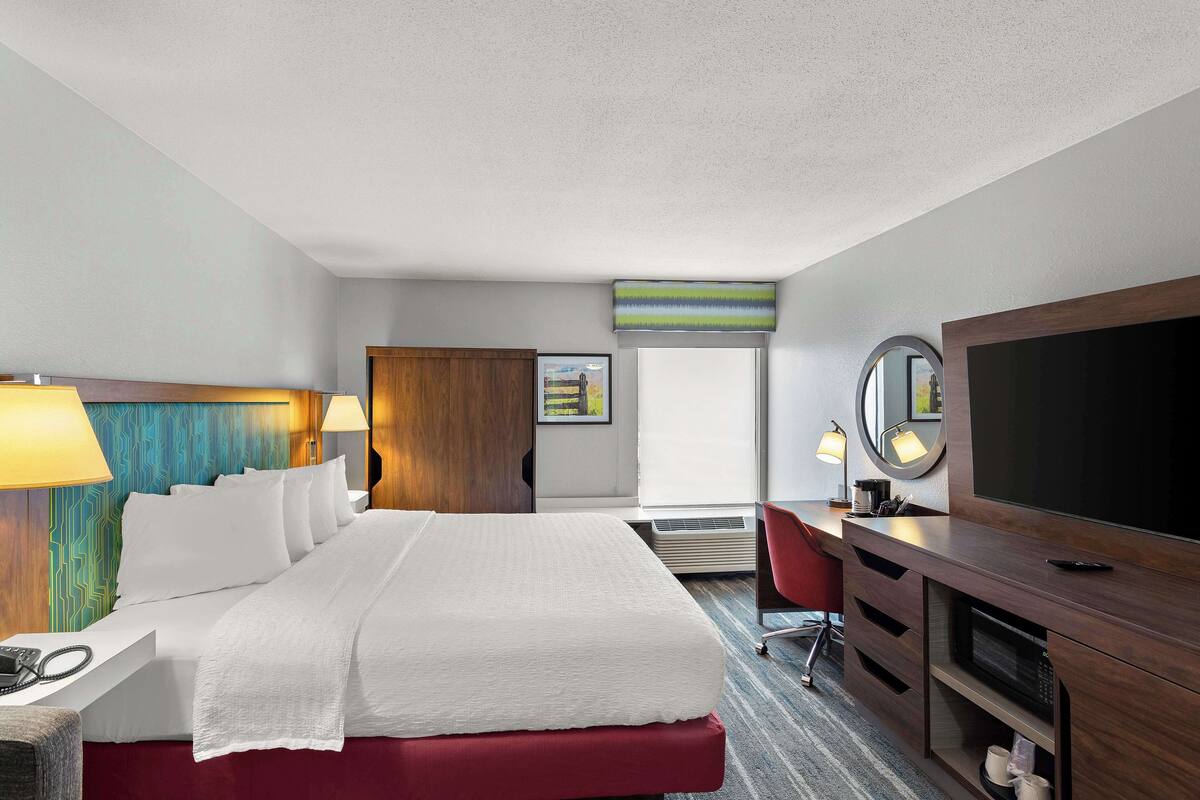 A hotel room with a bed, a desk with a computer, a TV, and a mirror.