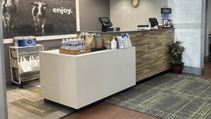 A hotel reception area with a reception desk, a clock on the wall, a digital kiosk, and a large poster with cows. - Hampton Inn Bridgeport/Clarksburg (Bridgeport)