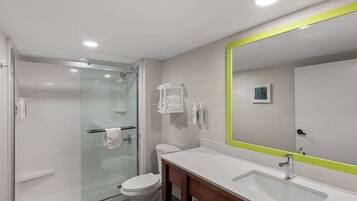 A modern bathroom with a glass shower enclosure, a white toilet, and a large mirror with a green frame.