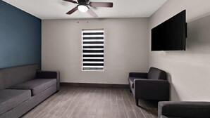 A room with a ceiling fan, a window with blinds, a flat-screen TV mounted on the wall, and a dark-colored sofa. - Econo Lodge Inn & Suites Laredo - Nuevo Laredo (Laredo)