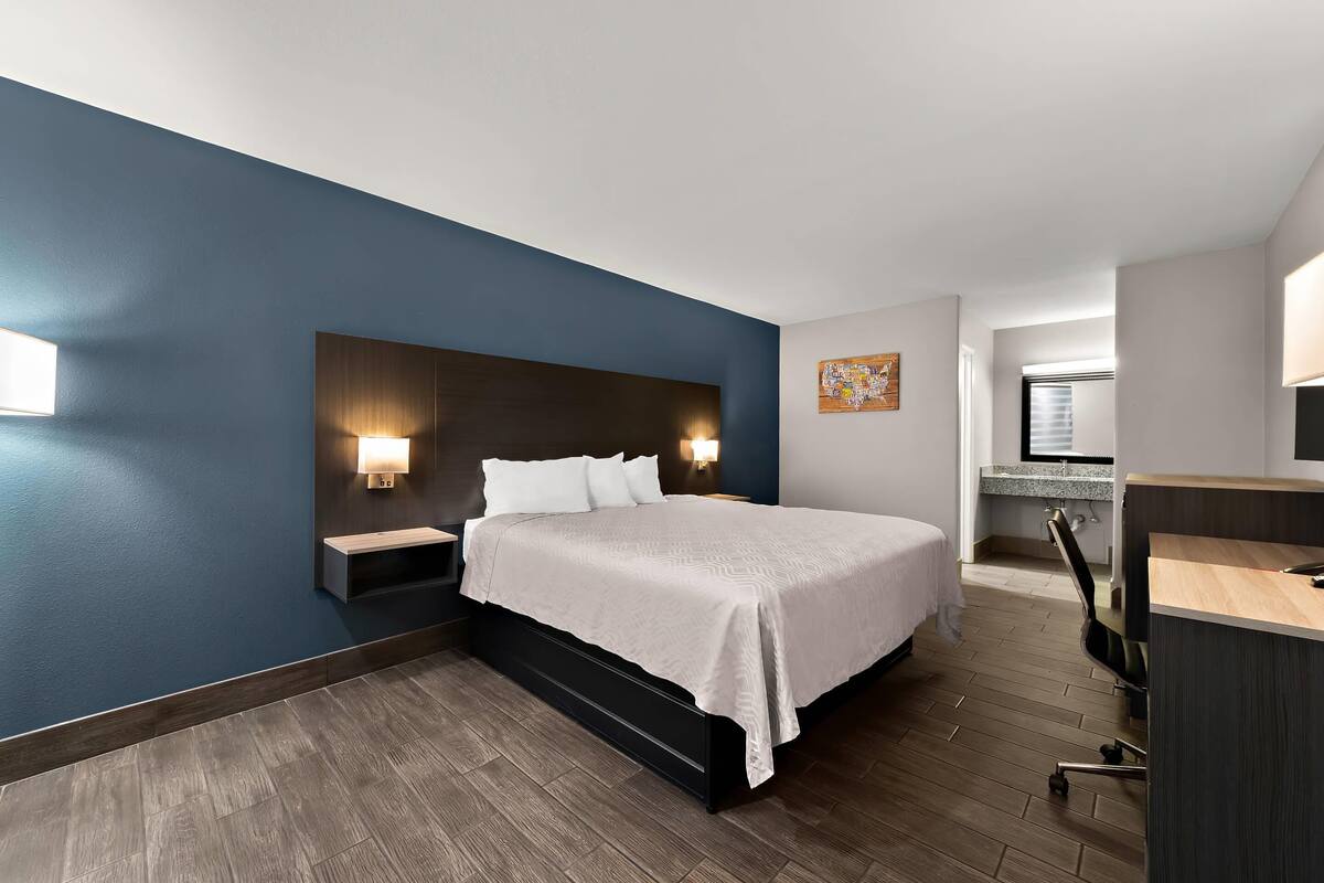 A modern hotel room with a large bed, bedside tables, a desk, and a chair.