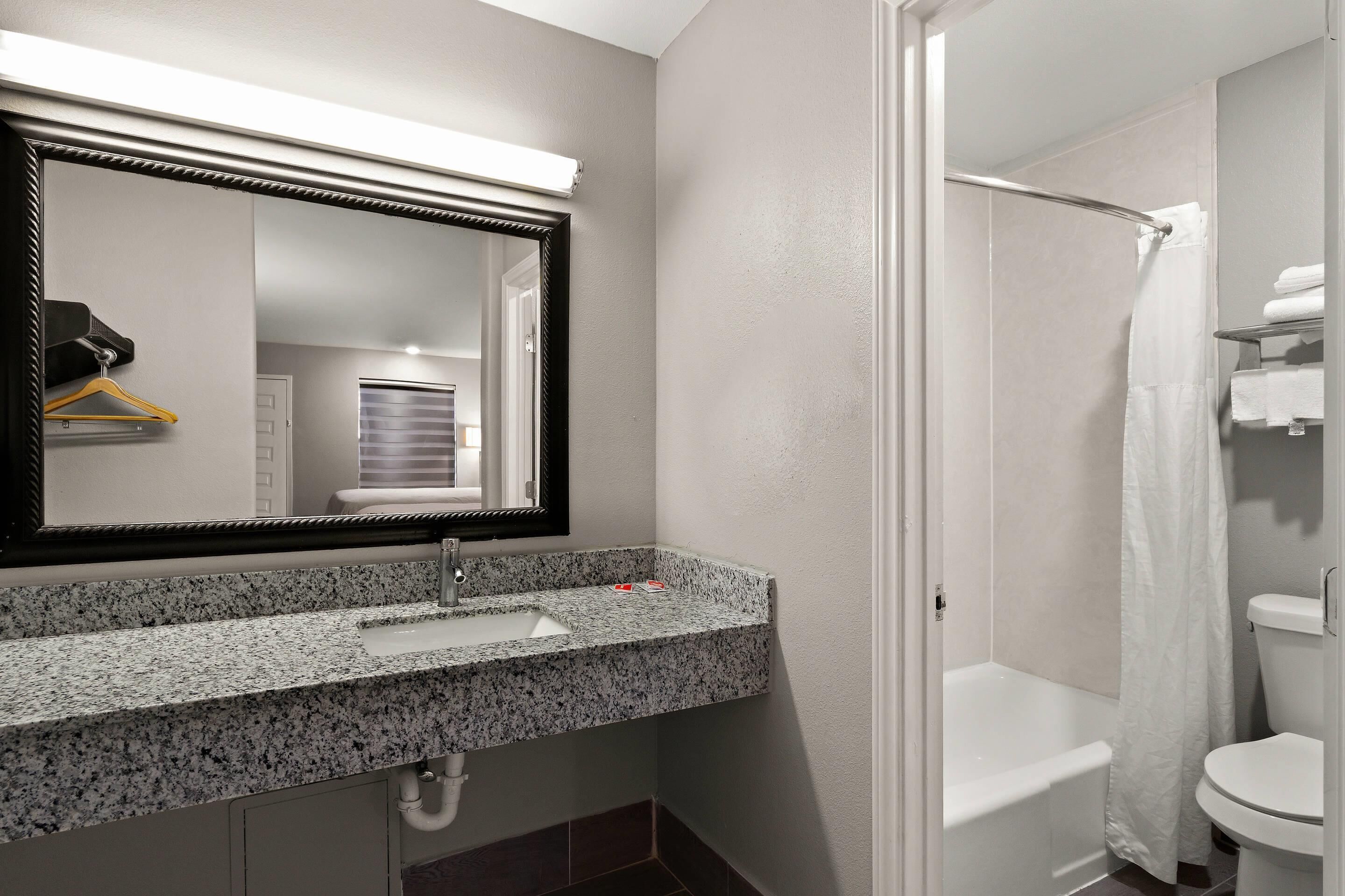 Un baño con lavamanos de encimera de granito, un espejo, una ducha y un inodoro.