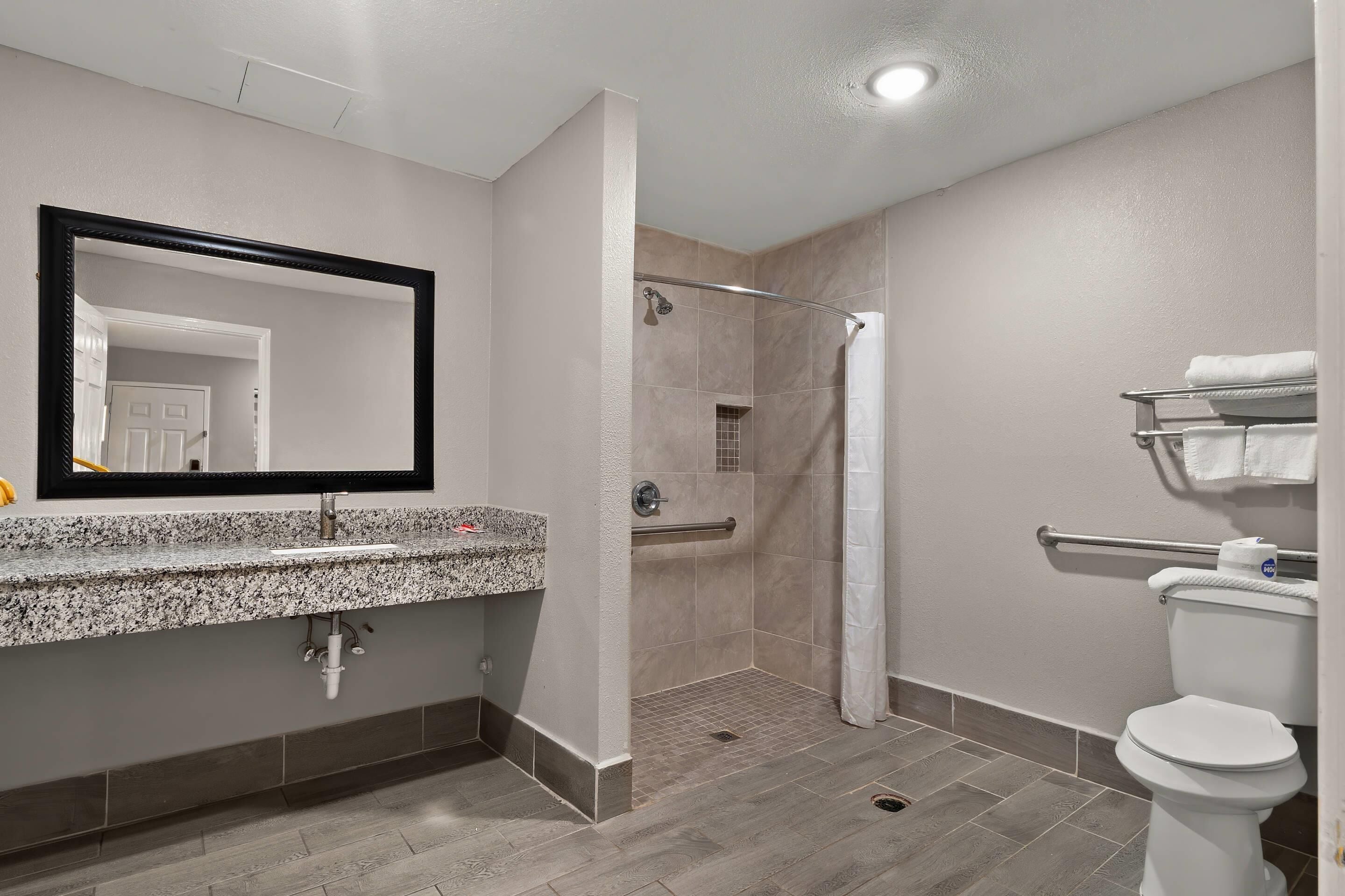 Un baño moderno con lavamanos de granito, ducha con puerta de vidrio y retrete con barandilla.
