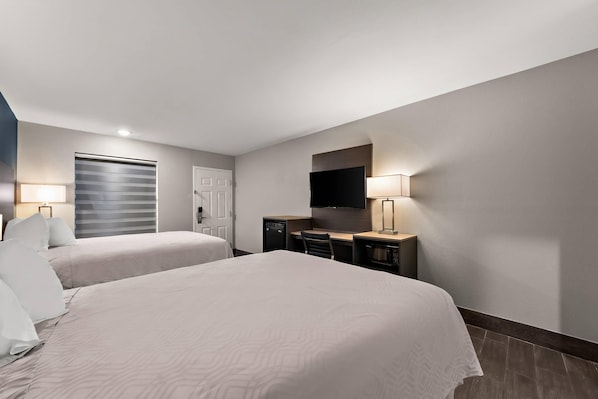 Une chambre d’hôtel avec deux lits, un bureau, une chaise, une télévision et une porte.
