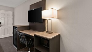 A hotel room with a wooden desk, a flat-screen TV mounted on the wall, a modern lamp, a black chair, and a built-in dishwasher. - Econo Lodge Inn & Suites Laredo - Nuevo Laredo (Laredo)