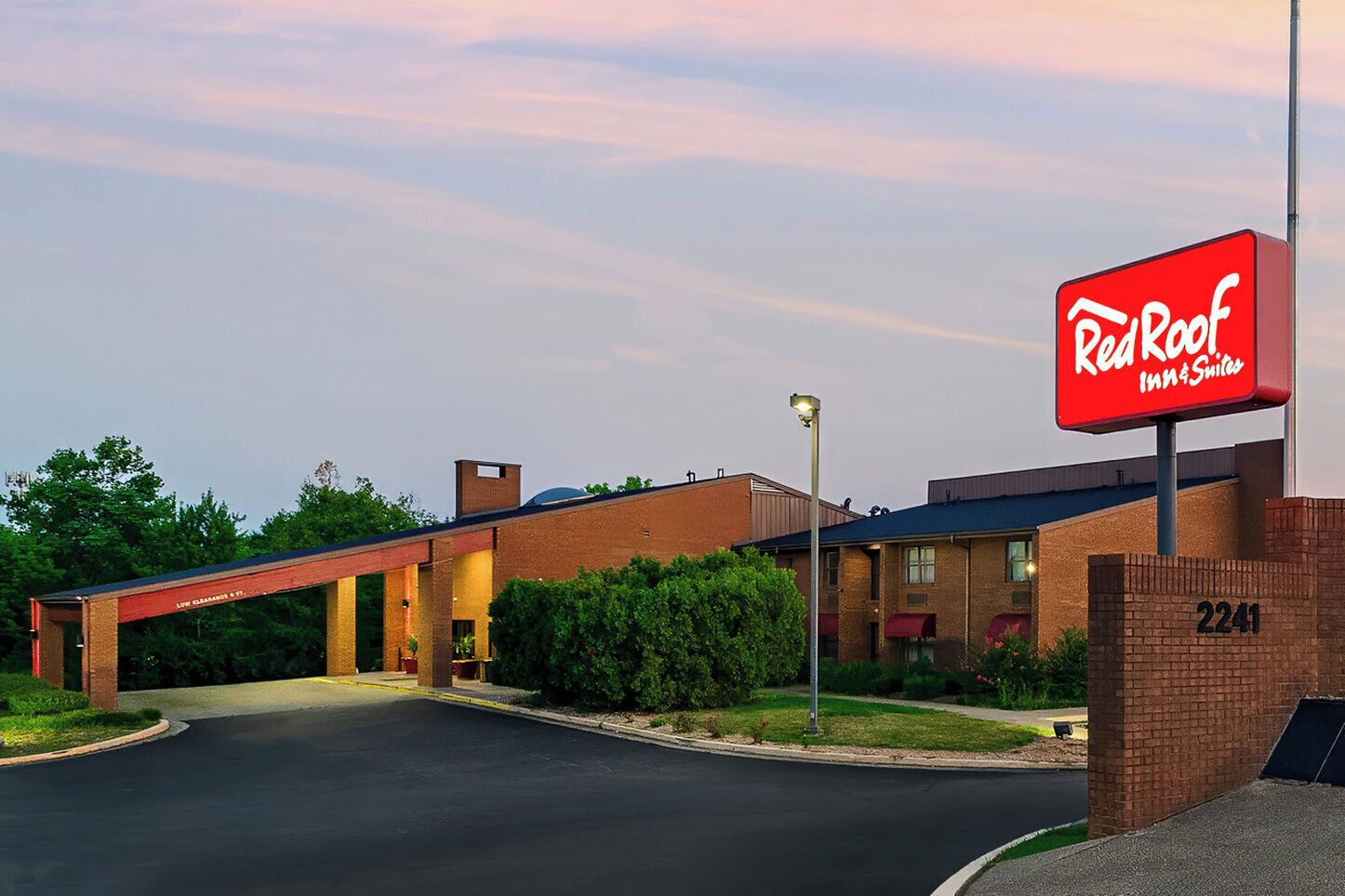 Un Red Roof Inn & Suites con fachada de ladrillo, una zona de estacionamiento techada y un cielo despejado.