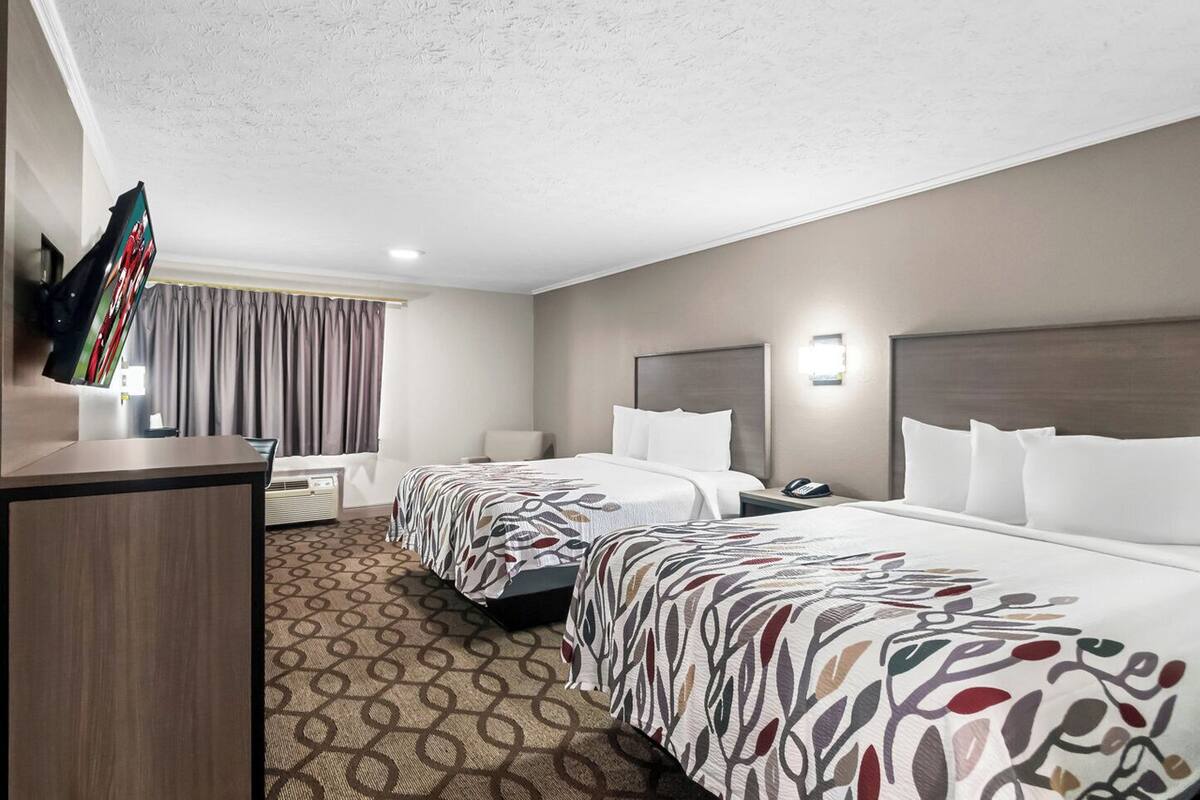 Une chambre d’hôtel avec deux lits, un bureau, une télévision et une fenêtre avec des rideaux.