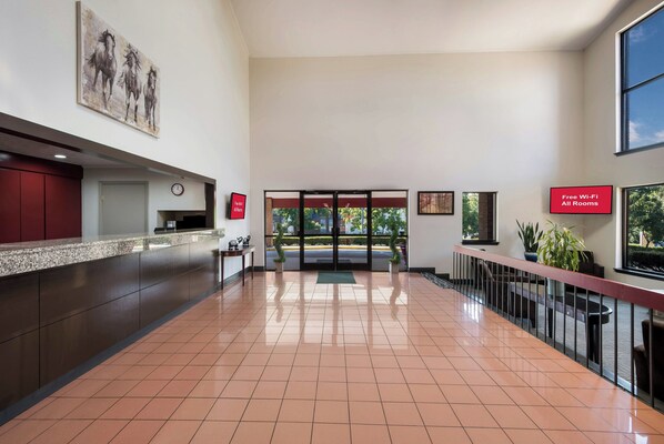 A hotel lobby with a reception desk, a clock, a sign indicating free Wi-Fi, and a large window with a view of trees.