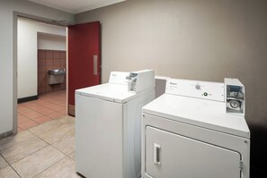 A laundry area with two front-loading washers and dryers, a red door, and a tiled floor. - Red Roof Inn & Suites Lexington - Hamburg (Lexington)