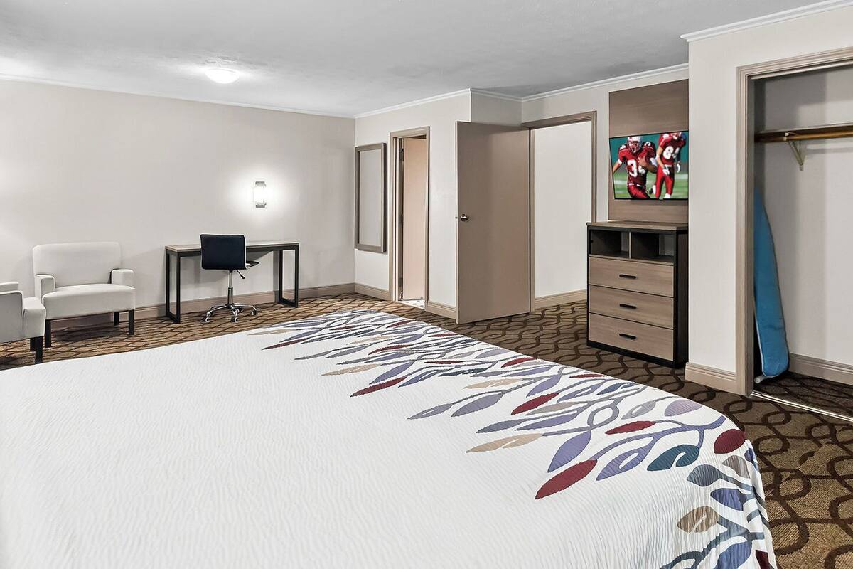 Une chambre d’hôtel avec un grand lit, un bureau, une chaise, une armoire et un téléviseur.