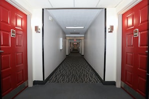 Un couloir d’hôtel avec des portes rouges numérotées 212 et 213, un sol recouvert de moquette et un luminaire au plafond.
