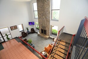 A spacious living area with a stone fireplace, large windows, and a view of the outdoors. - Red Roof Inn & Suites Lexington - Hamburg (Lexington)