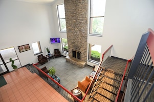 Amplia sala de estar con chimenea de piedra, ventanas grandes y vistas al exterior.