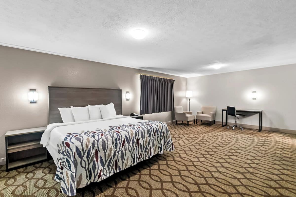 Une chambre d’hôtel avec un grand lit, deux fauteuils, un bureau et une lampe.