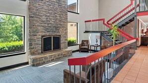 A spacious interior with a stone fireplace, a red staircase, and a view of greenery outside. - Red Roof Inn & Suites Lexington - Hamburg (Lexington)