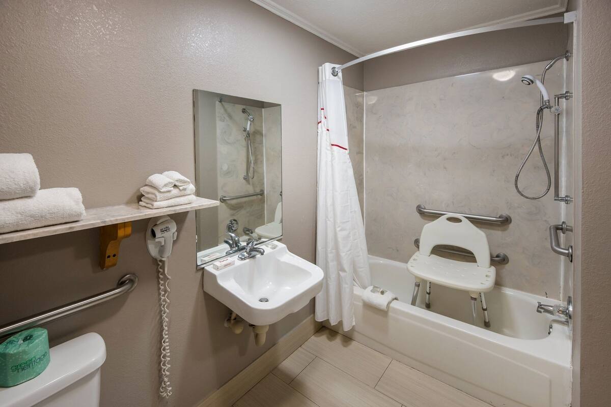 Une salle de bain équipée d’un lavabo, d’un miroir, d’un porte-serviettes, d’une douche et de toilettes.