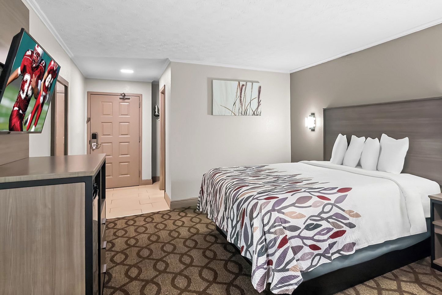 A hotel room with a bed, a desk, a TV, and a door.
