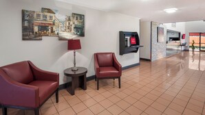 A hotel lobby with two leather armchairs, a small round table, a lamp, and a wall-mounted TV.