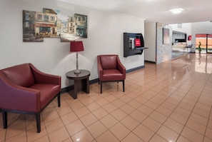 Un hall d’hôtel avec deux fauteuils en cuir, une petite table ronde, une lampe et un téléviseur fixé au mur.