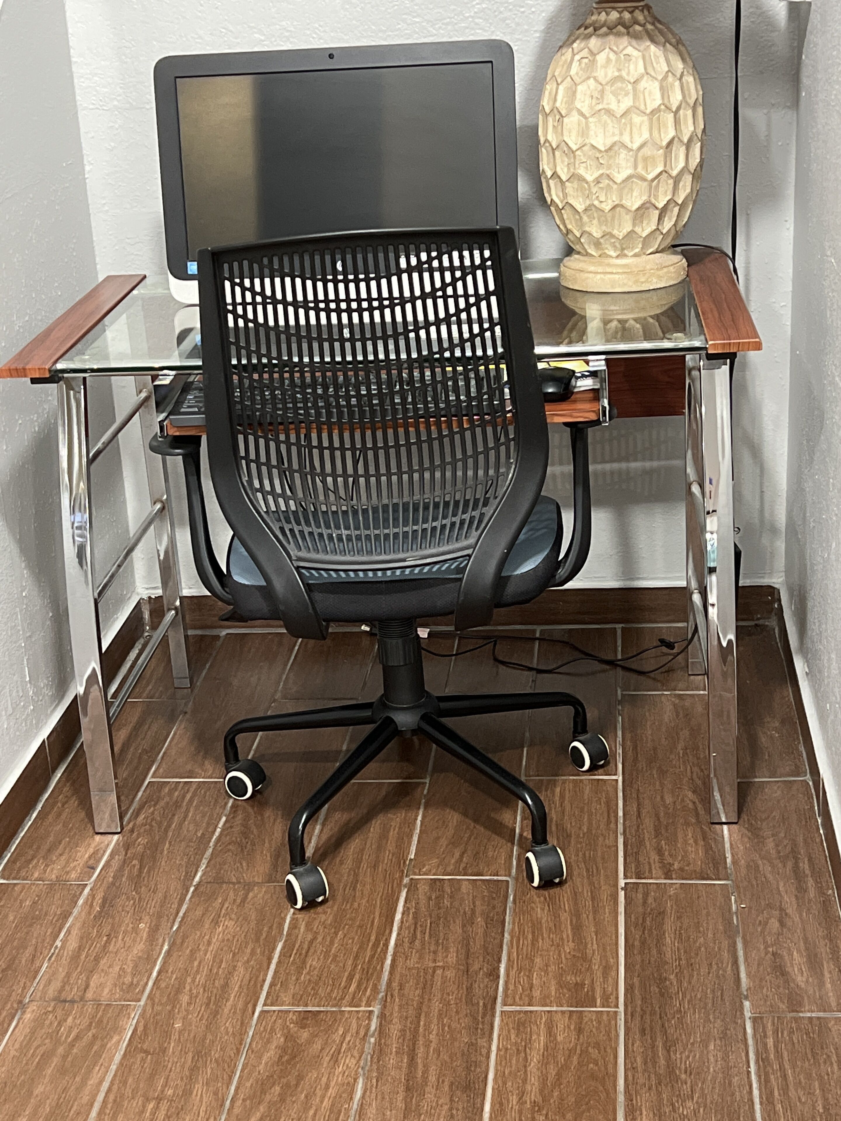 Un fauteuil de bureau moderne, doté d’un dossier en tissu ajouré et de roulettes, posé sur un sol carrelé.