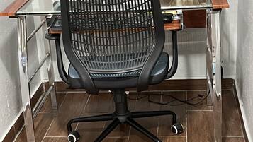Un fauteuil de bureau moderne, doté d’un dossier en tissu ajouré et de roulettes, posé sur un sol carrelé.