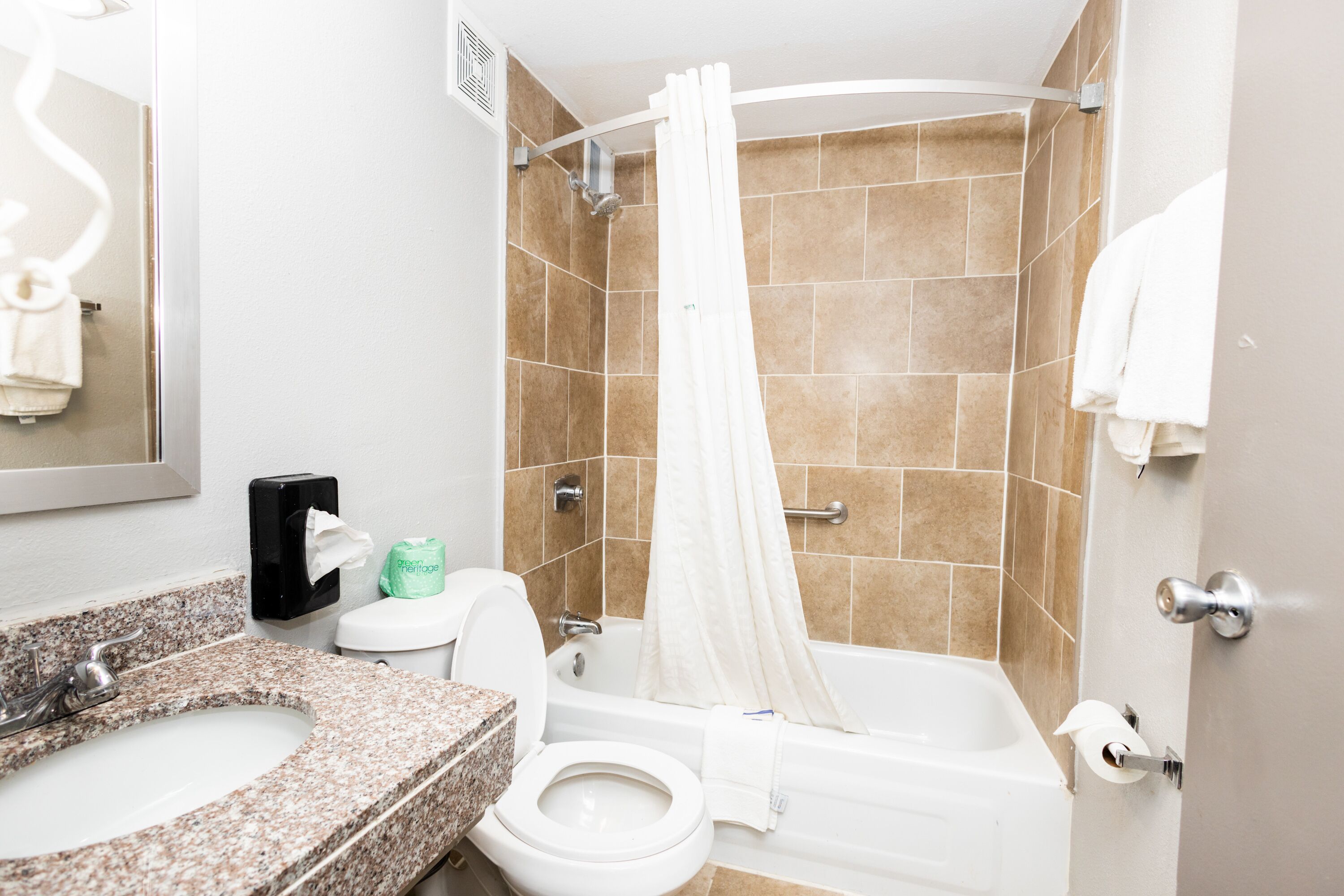 A bathroom with a granite countertop sink, a toilet, a bathtub with a shower curtain, and a towel rack.