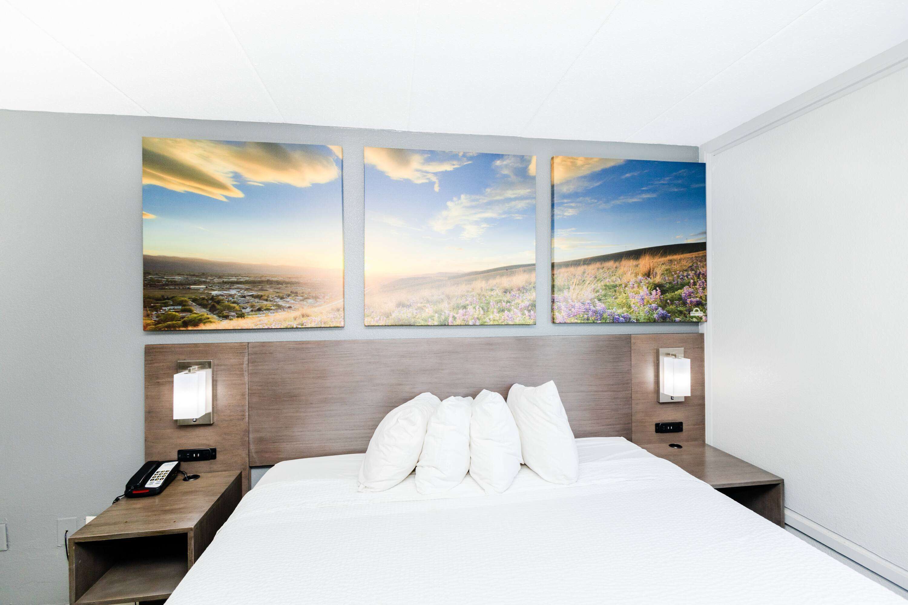 A hotel room with a large bed, three wall-mounted paintings, bedside lamps, and a bedside phone.