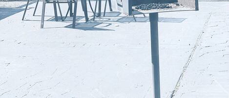 An outdoor seating area with metal chairs and a table, a grill, and a fence in the background.
