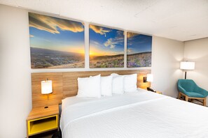 A hotel room with a large bed, a wooden headboard, a nightstand with a lamp, a chair, and a wall-mounted telephone. - Days Inn by Wyndham Sharonville (Sharonville)